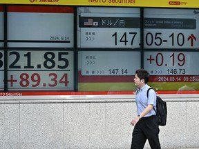 A man walks past a brokerage display showing the early numbers (L) on the Tokyo Stock Exchange as well as the Japanese yen versus US dollar (R), along a street in Tokyo on Aug. 14, 2024.