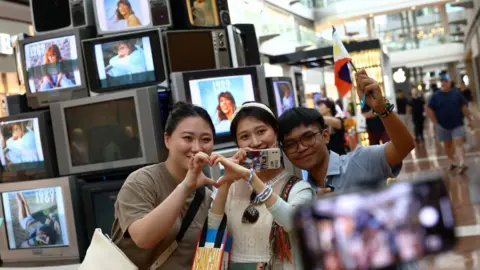 EPA Fans, one holding a Philippines flag, pose for a picture in front of a Taylor Swift installation in Marina Bay Sands shopping mall in Singapore