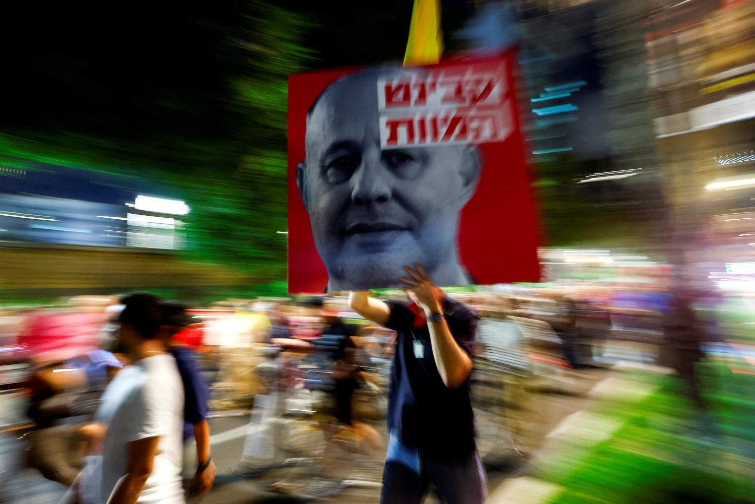 A person holds a placard with the face of Israel's National Security Advisor Tzachi Hanegbi, as women lead a march for the return of hostages kidnapped a year ago. REUTERS